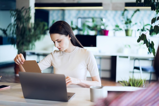 Young attractive businesswoman making notes in notepad at her working place