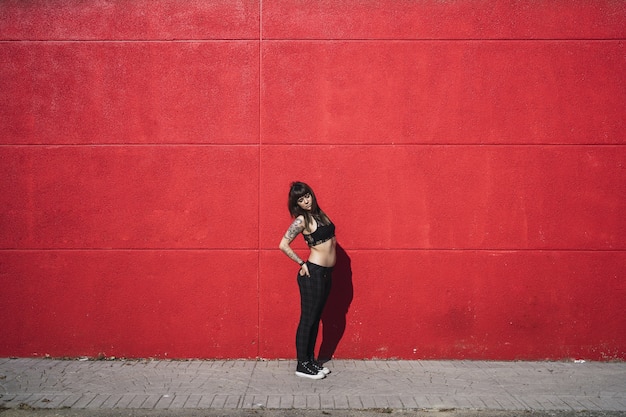 Free Photo young attractive caucasian female with tattoos standing against a red wall