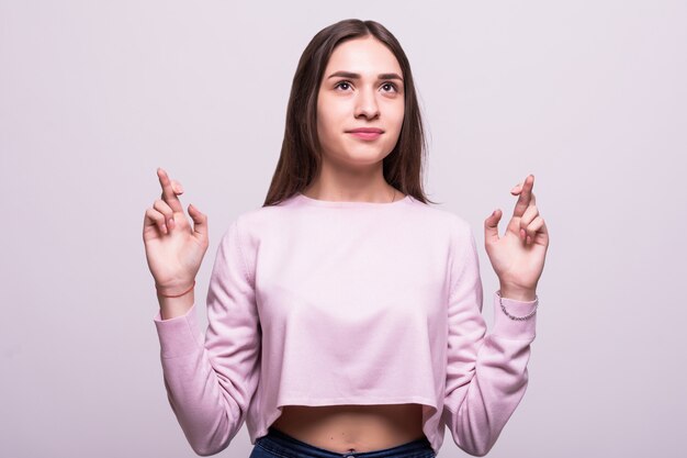 Young attractive female holds her fingers crossed , wishful thinking, studio shoot isolated on white background