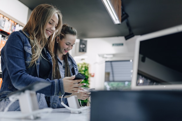 Free photo young attractive girls in electronics shop testing phones on a shop window. concept of buying gadgets.