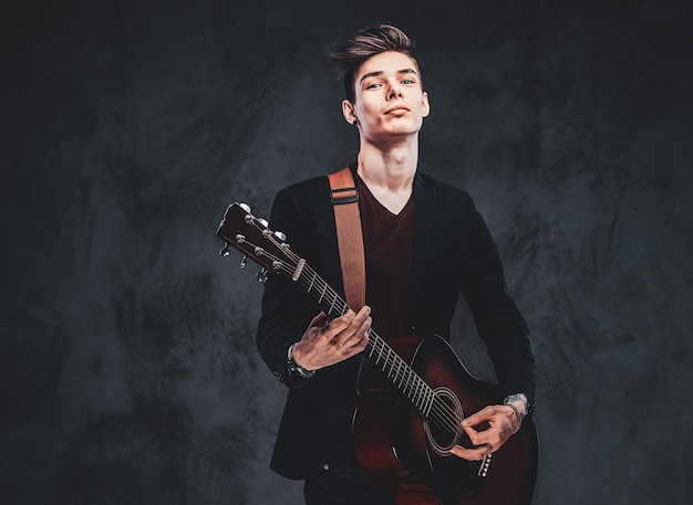 Young attractive man is playing acoustic guitar at studio while posing for photographer.