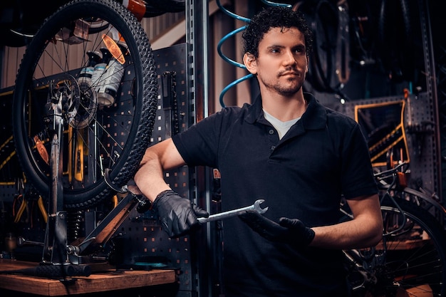 Young attractive mechanic is posing next to bicycle at his own workshop.