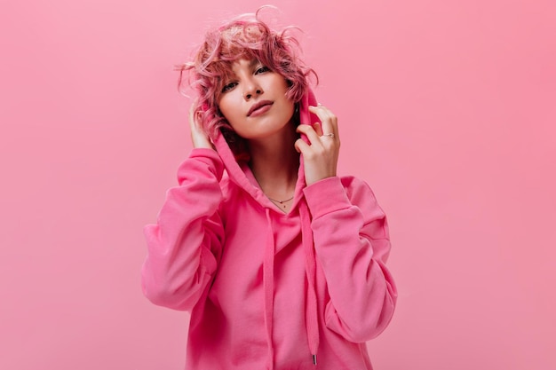 Free Photo young attractive pinkhaired woman in bright fuchsia hoodie looks into camera and poses with smile on isolated background