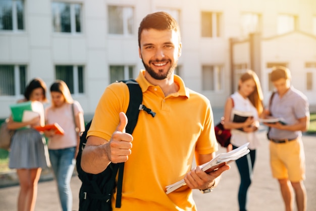 Free photo young attractive smiling student showing thumb up outdoors on campus at the university.