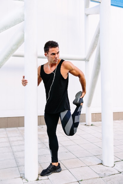 Young attractive sportsman in headset doing sports stretching exercises during workout