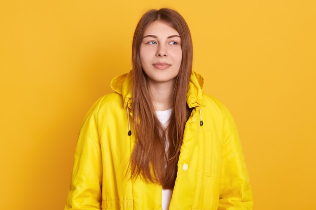 Free Photo young attractive student girl wearing jacket, having beautiful straight hair, standing against yellow wall, looks thoughtful.