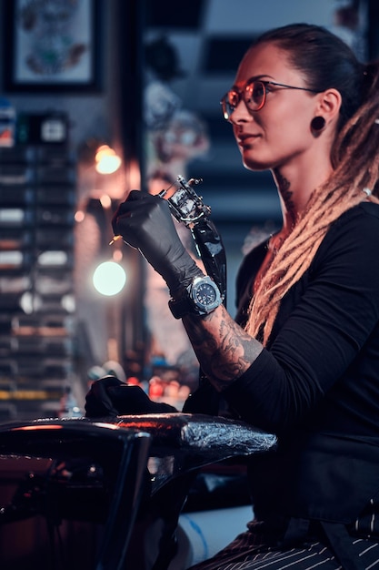 Free photo young attractive tattoo artist in black gloves is tuning her tattoo machine before tattoo session.