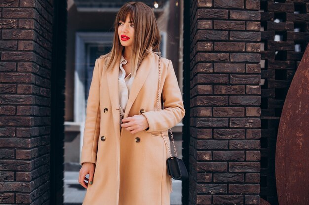 Young attractive woman in beige coat posing in the street