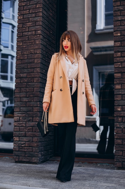 Free photo young attractive woman in beige coat posing in the street