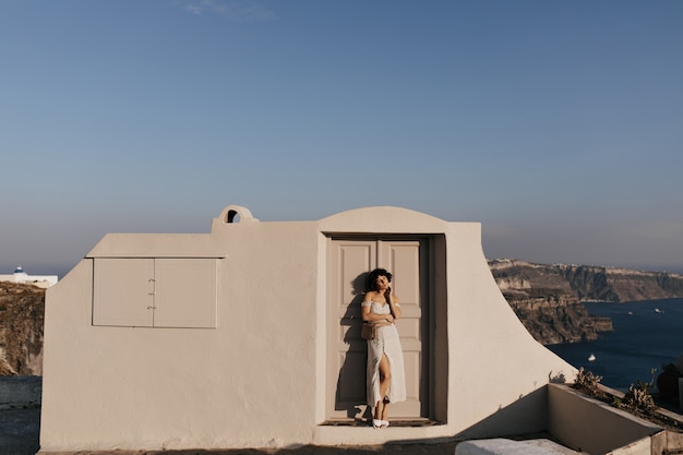 Free photo young attractive woman in midi dress poses near beige house