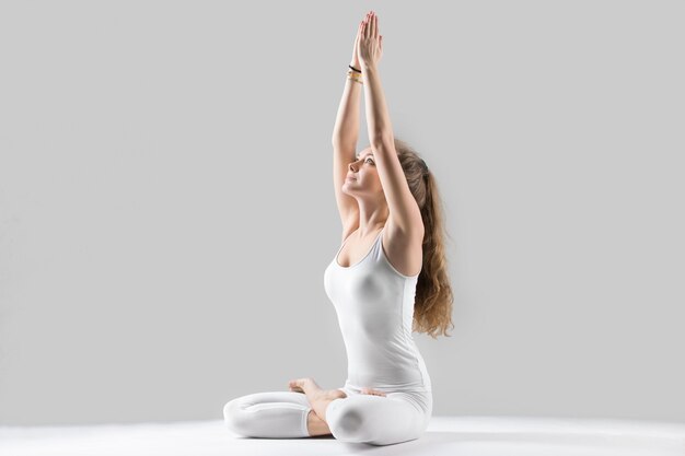 Young attractive woman sitting in Padmasana pose, grey studio ba