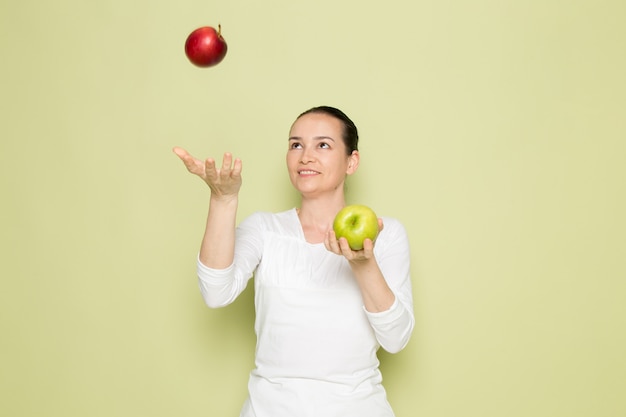 Young attractive woman in white shirt smiling and playing with green and red apples