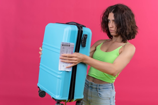 A young attractive woman with short hair wearing green crop top showing blue suitcase with plane tickets