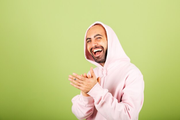 Young bald caucasian man in pink hoodie isolated, happy clapping and applauding happy and joyful, smiling proud hands together