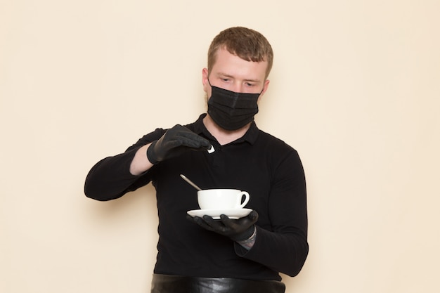 young barista in black working suit with ingredients and coffee equipment brown coffee seeds wearing black sterile mask on white