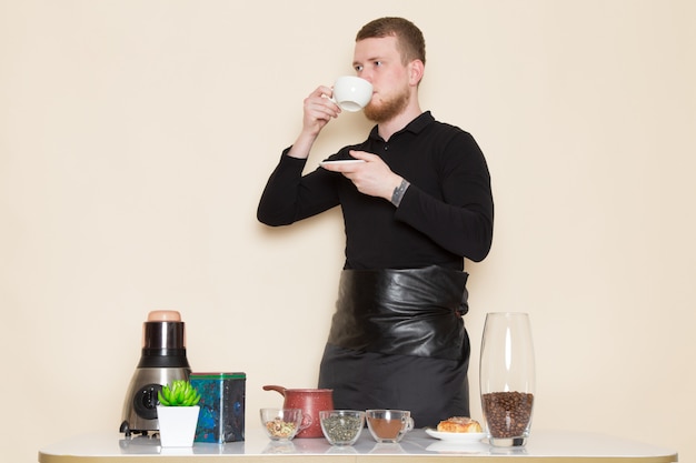 young barista in black working suit with ingredients and coffee equipment brown coffee seeds on white