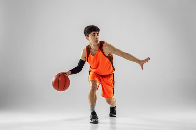 Young basketball player of team wearing sportwear training, practicing in action, motion in run isolated on white wall