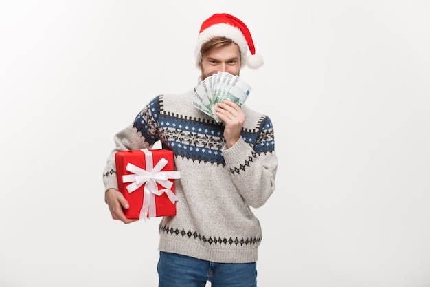 young beard man holding a christmas gift box and money on white