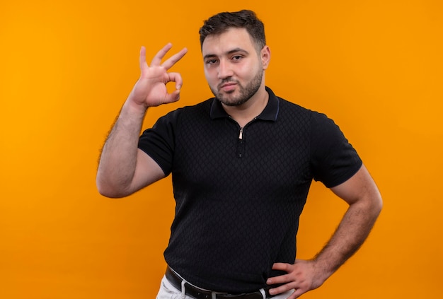 Free photo young bearded man in black shirt  smiling confident doing ok sign