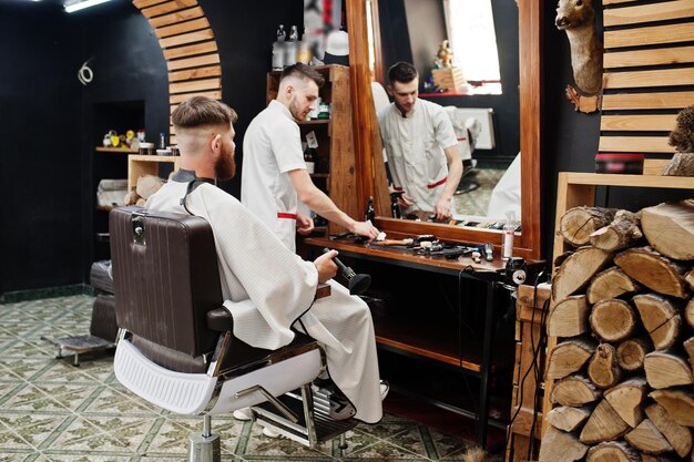 Young bearded man getting haircut by hairdresser while sitting in chair at barbershop Barber soul