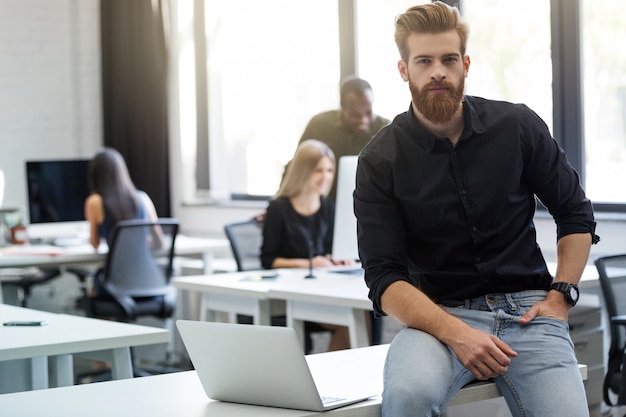 Free photo young bearded man sitting on his desk in an office