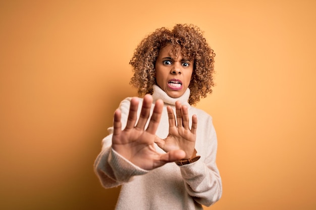 Free photo young beautiful african american woman wearing turtleneck sweater over yellow background afraid and terrified with fear expression stop gesture with hands shouting in shock panic concept