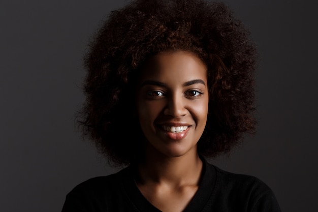 Young beautiful african girl smiling over dark wall