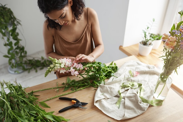 Young beautiful african woman florist taking care of flowers at workplace.