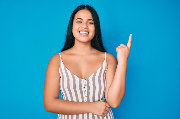 Young beautiful asian girl wearing casual clothes with a big smile on face, pointing with hand and finger to the side looking at the camera.