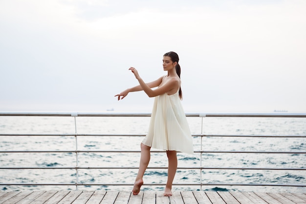 Free photo young beautiful ballerina dancing and posing outside, sea wall