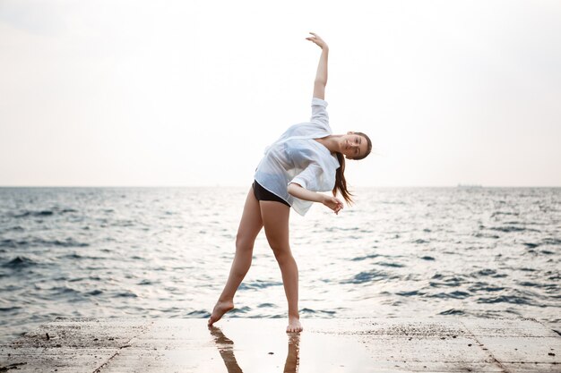 Young beautiful ballerina dancing and posing outside, sea wall