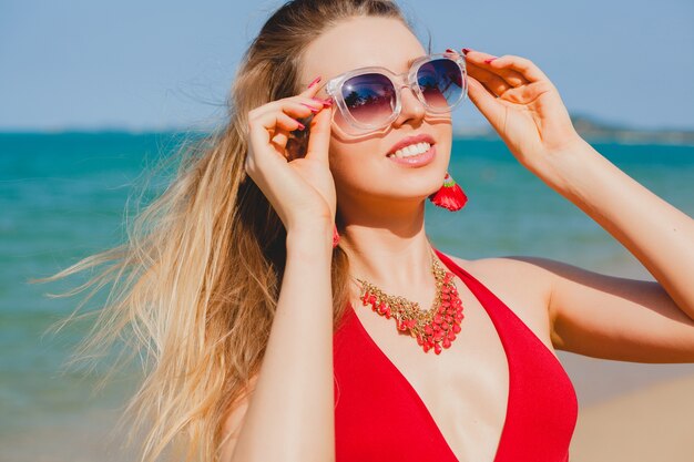 Young beautiful blond woman sunbathing on beach in red swimming suit, sunglasses