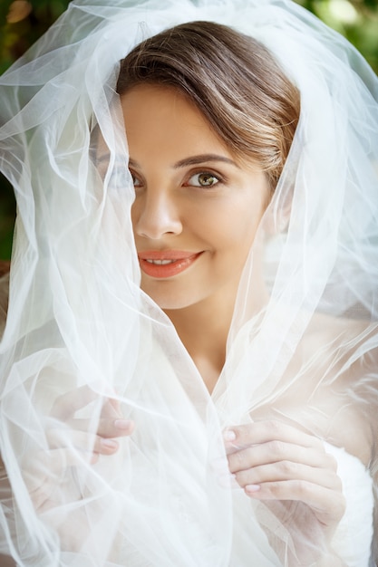 Young beautiful blonde bride in wedding dress and veil smiling.