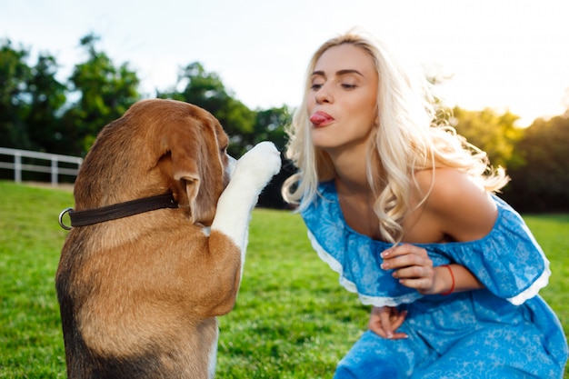 Young beautiful blonde girl walking, playing with beagle dog in park.