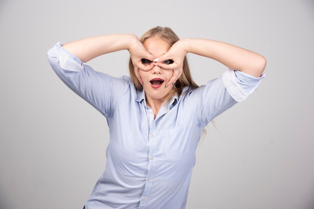 Young beautiful blonde woman doing ok gesture like binoculars and looking through fingers.