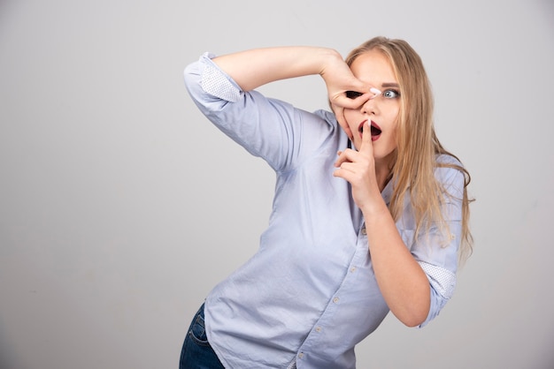 Young beautiful blonde woman looking through fingers and doing silent gesture.