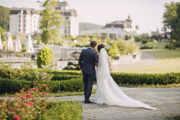 A young and beautiful bride and her husband standing in a park with bouquet of flowers