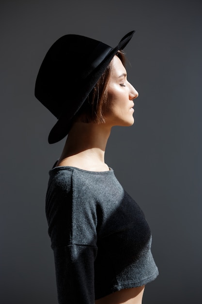 Young beautiful brunette girl in black hat standing in profile.