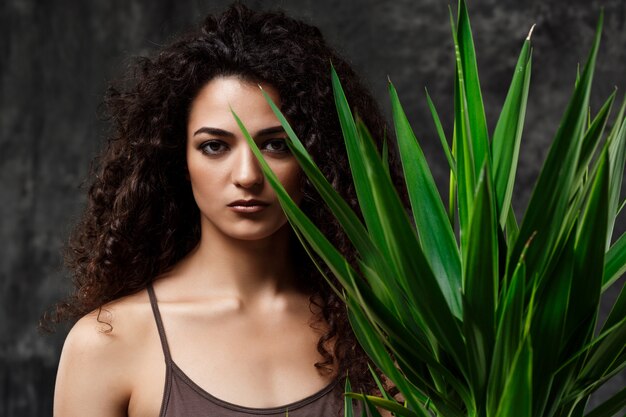 Young beautiful brunette girl in tropical plants over grey wall