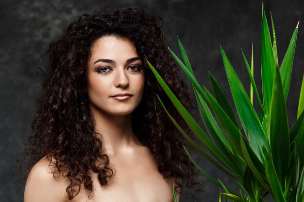 Young beautiful brunette girl in tropical plants over grey wall