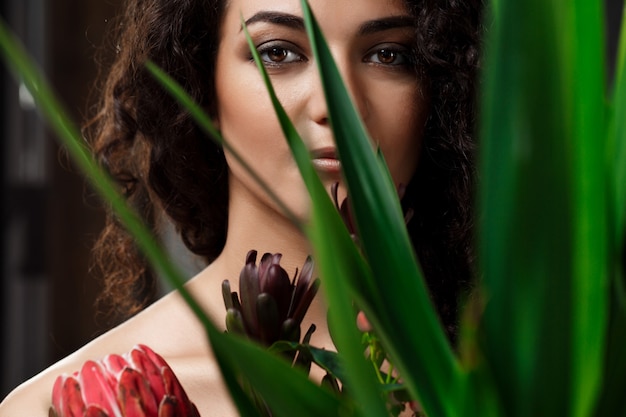 Young beautiful brunette girl in tropical plants over grey wall