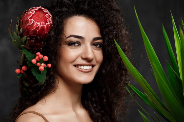 Young beautiful brunette girl in tropical plants over grey wall