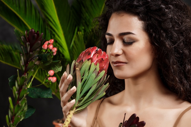 Free photo young beautiful brunette girl in tropical plants over grey wall