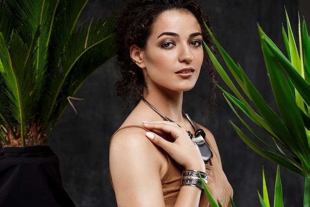 Young beautiful brunette girl in tropical plants over grey wall