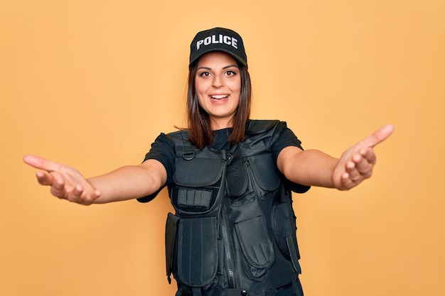 Free Photo young beautiful brunette policewoman wearing police uniform bulletproof and cap smiling cheerful offering hands giving assistance and acceptance