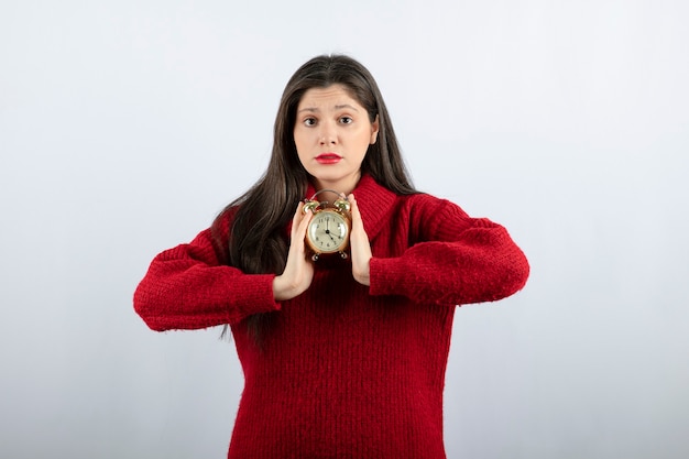 Free photo young beautiful brunette woman holding an alarm clock standing over white background