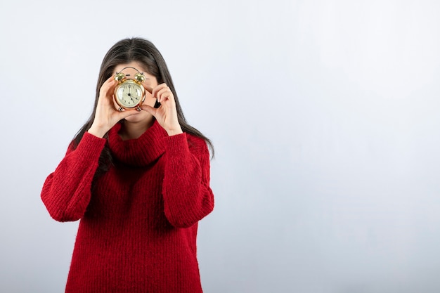 Free photo young beautiful brunette woman holding an alarm clock standing over white background