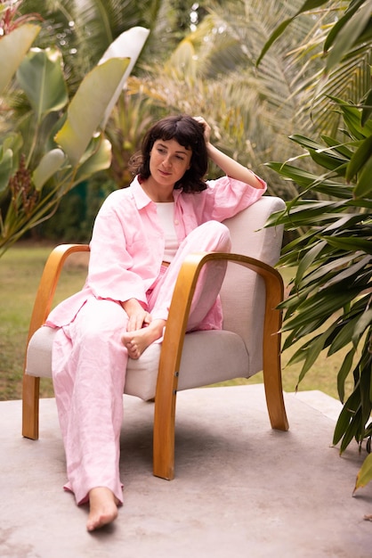 Free photo young beautiful brunette woman in pink clothes sits on chair outdoors summer day nature concept