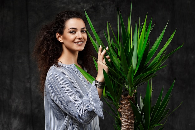 Free photo young beautiful brunette woman in tropical plants over grey wall