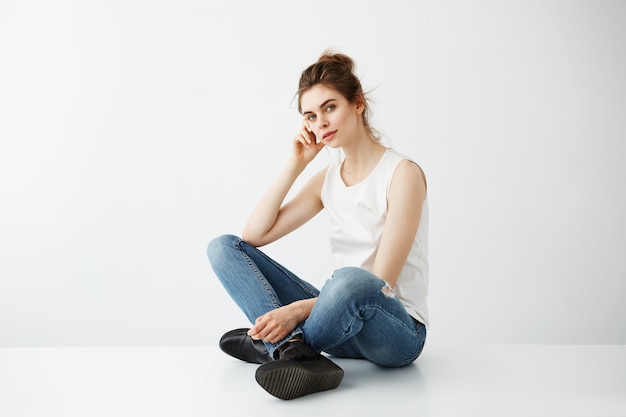 Young beautiful brunette woman with bun smiling sitting over white background.